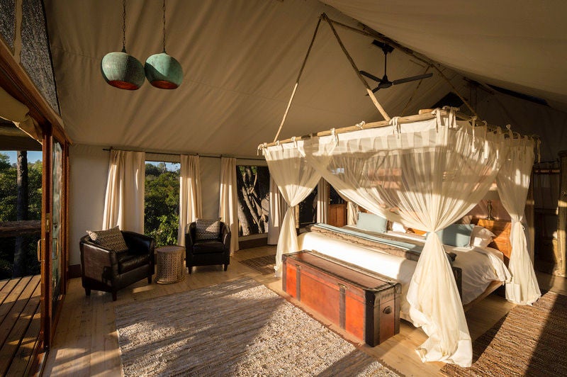 Elevated luxury tent lodge with wooden deck overlooking Okavango Delta wetlands, surrounded by lush African wilderness at sunset