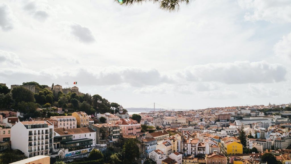 Small wooden boat cruising past pastel-colored historic buildings along Lisbon's waterfront at sunset, with iconic cable cars nearby