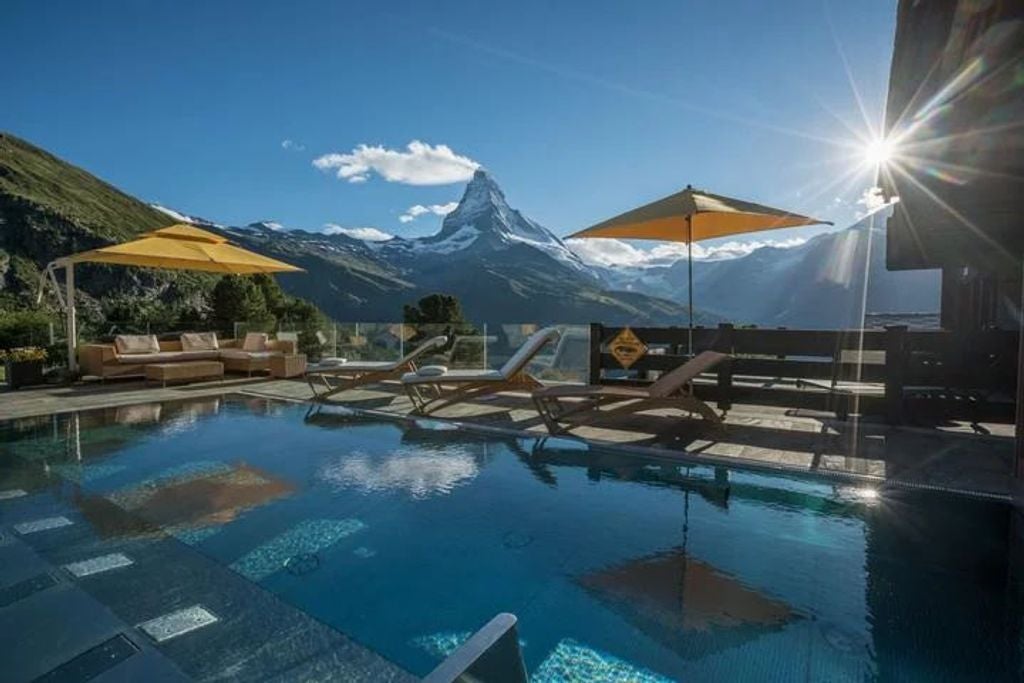 Luxury alpine hotel with wooden balconies nestled in snowy Swiss mountains, panoramic Matterhorn views, illuminated at dusk