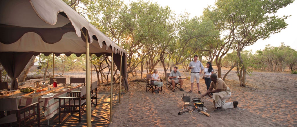 Luxury safari tent set against an African savanna backdrop with acacia trees, golden sunlight, and a private wooden deck porch