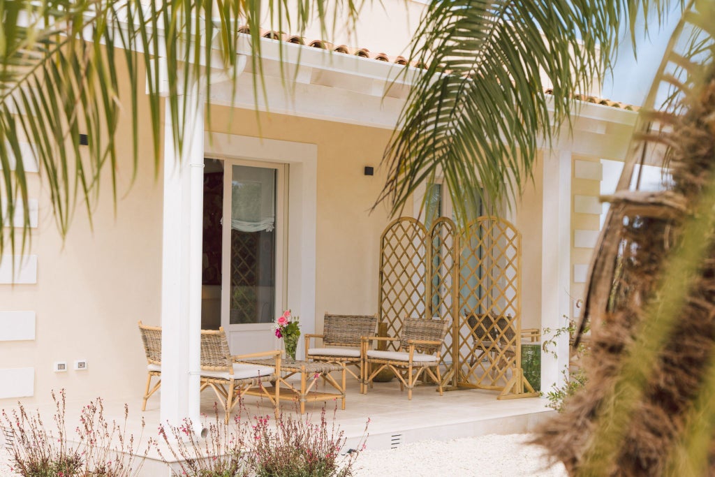 Elegant Sicilian luxury suite with soft cream walls, ornate headboard, plush white linens, and traditional wooden furnishings overlooking verdant landscape