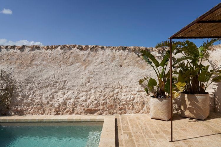 Rustic luxury bedroom in stone-walled Masseria Calderisi, featuring crisp white linens, wooden furniture, and soft natural light from arched window