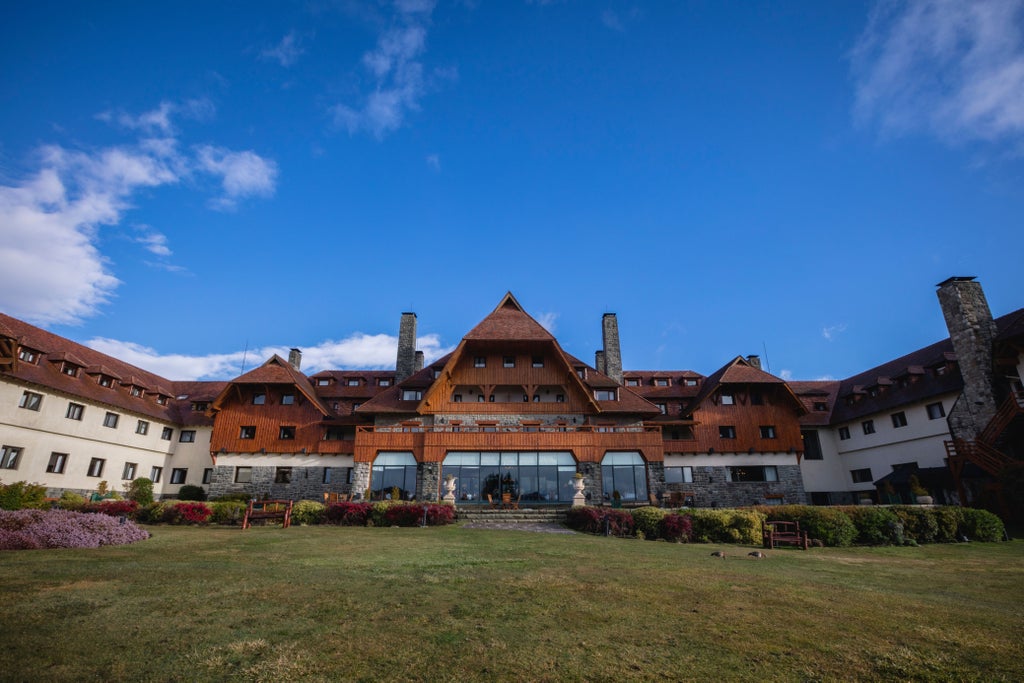 Luxurious mountain resort with Swiss chalet architecture nestled between lakes, surrounded by snow-capped Patagonian peaks at sunset