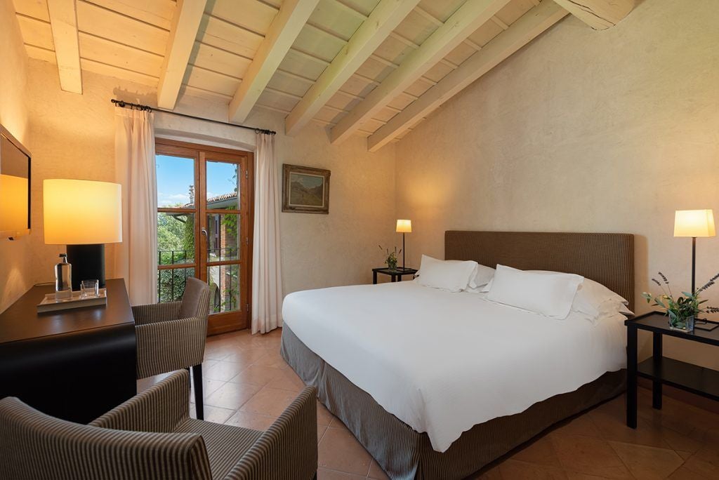 Elegant classic hotel room with lake view, soft neutral tones, plush white bedding, and refined wooden furniture at Villa Arcadio in Italy