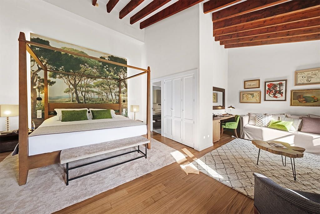 Elegant junior suite with crisp white bedding, wooden headboard, plush seating area, and large windows overlooking scenic countryside in Sóller, Spain