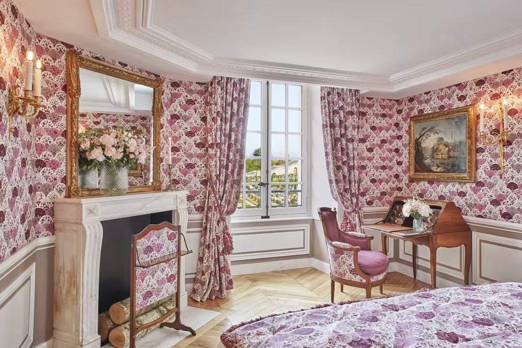 Opulent French palace hotel room with period furnishings, gold-framed mirror, crystal chandelier, and ornate wall moldings overlooking gardens