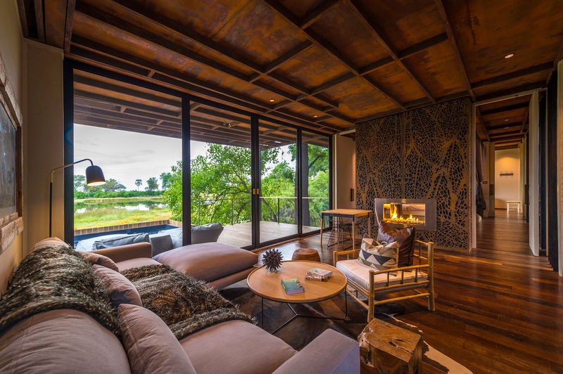 Elevated luxury safari lodge with thatched-roof villas overlooking the Okavango Delta, connected by wooden walkways at sunset