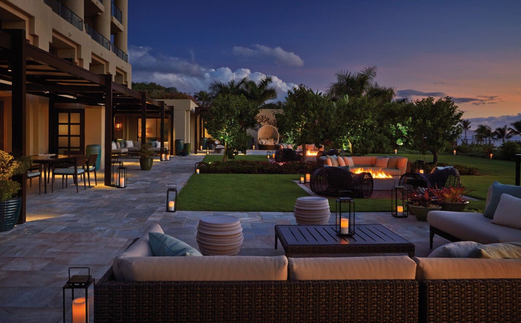 Luxurious oceanfront resort with infinity pools overlooking white sandy beach, palm trees and Pacific waters at sunset in Maui