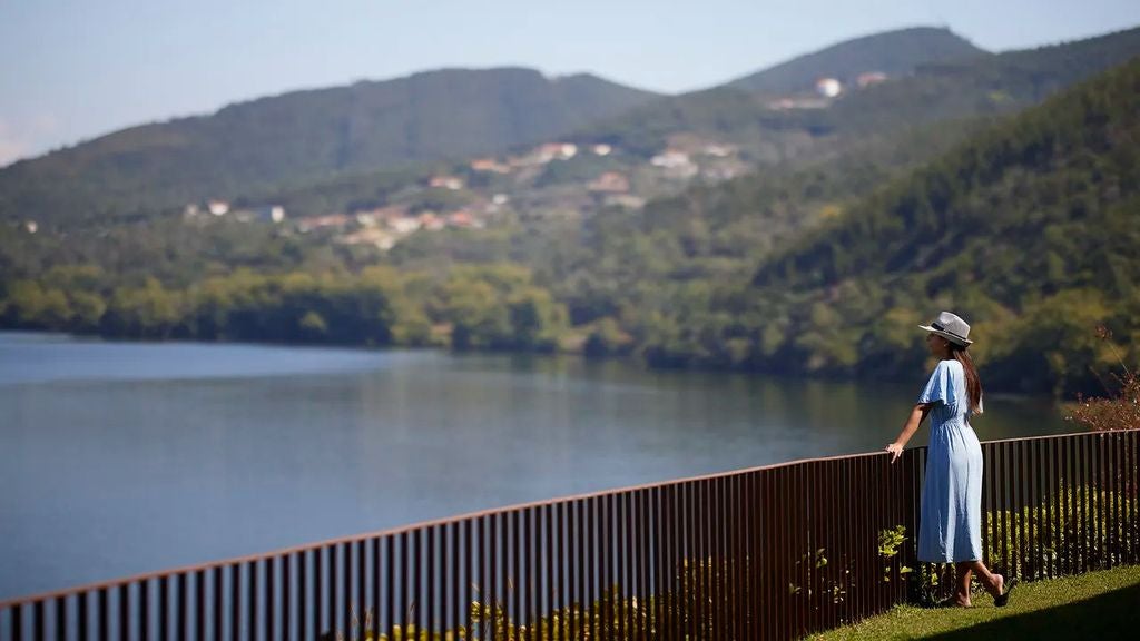 Modern infinity pool overlooking Douro Valley vineyards, with sleek lounge chairs and panoramic views of terraced hillsides at sunset