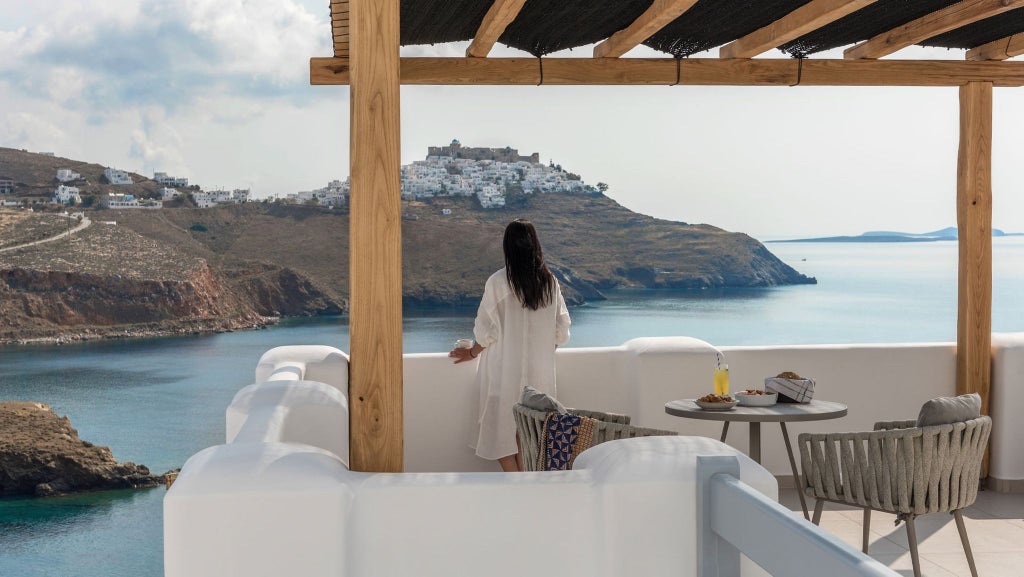 Elegant Greek honeymoon suite with white minimalist decor, panoramic sea view, luxurious king bed, and romantic sunset lighting from Aegean windows