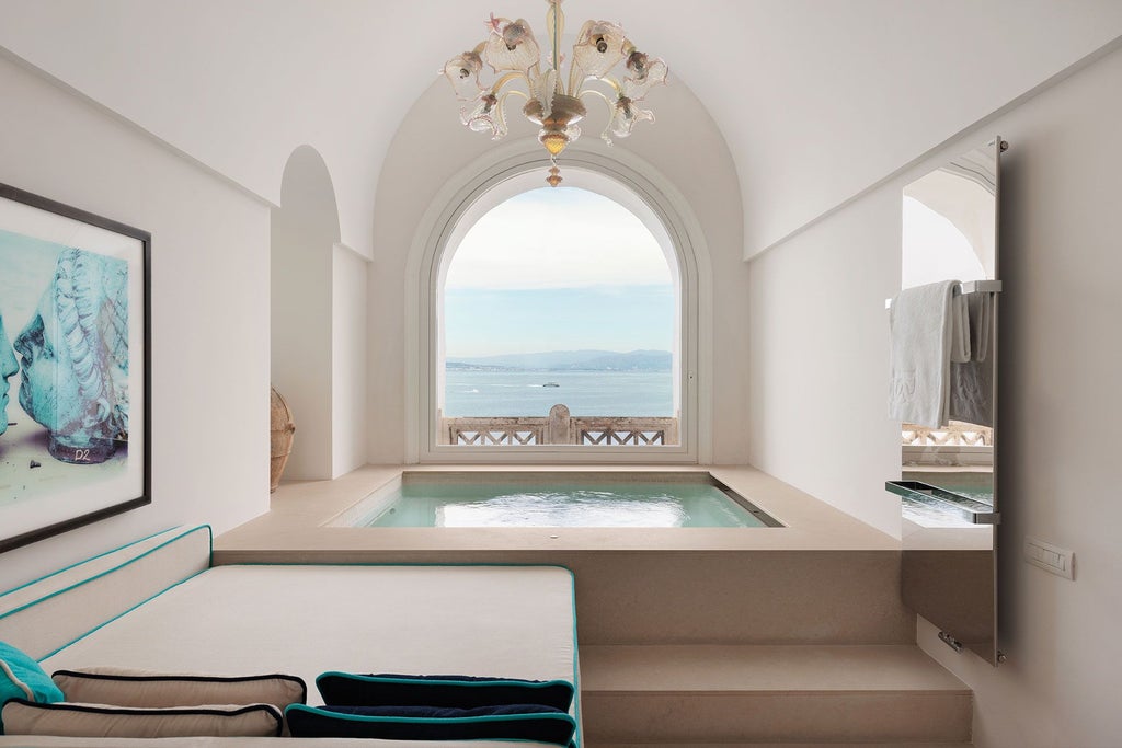 Elegant, sun-drenched suite with panoramic Amalfi Coast view, featuring marble floors, ornate furnishings, and floor-to-ceiling windows overlooking azure Mediterranean waters.