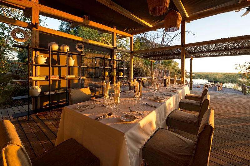 Elevated safari tent overlooking Botswana wilderness, featuring private deck, canvas walls and thatched roof amid lush savanna at sunset