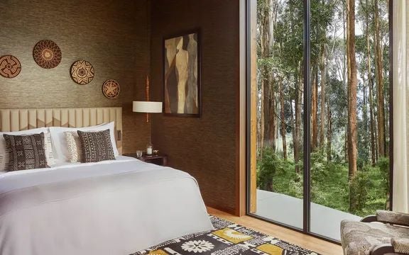 Luxurious Rwandan suite with floor-to-ceiling windows, contemporary African design, volcanic stone walls, and lush rainforest mountain backdrop