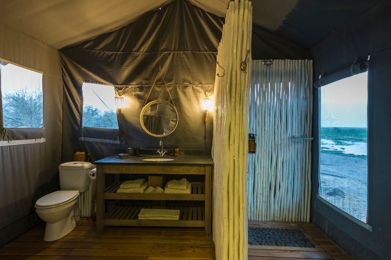 Elevated safari tent with private deck overlooking Linyanti wetlands at sunset, canvas walls and wooden furnishings blend with nature