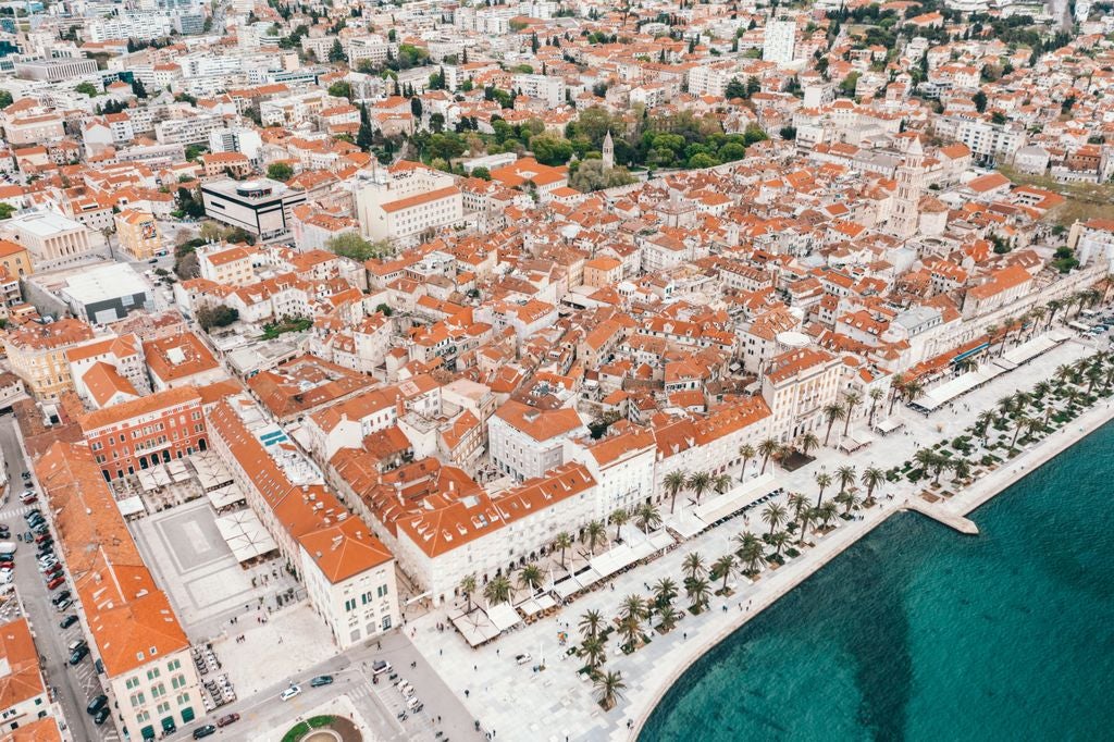 Aerial view of Split's medieval old town with red-tiled roofs, overlooking turquoise Adriatic waters and luxury yachts in marina