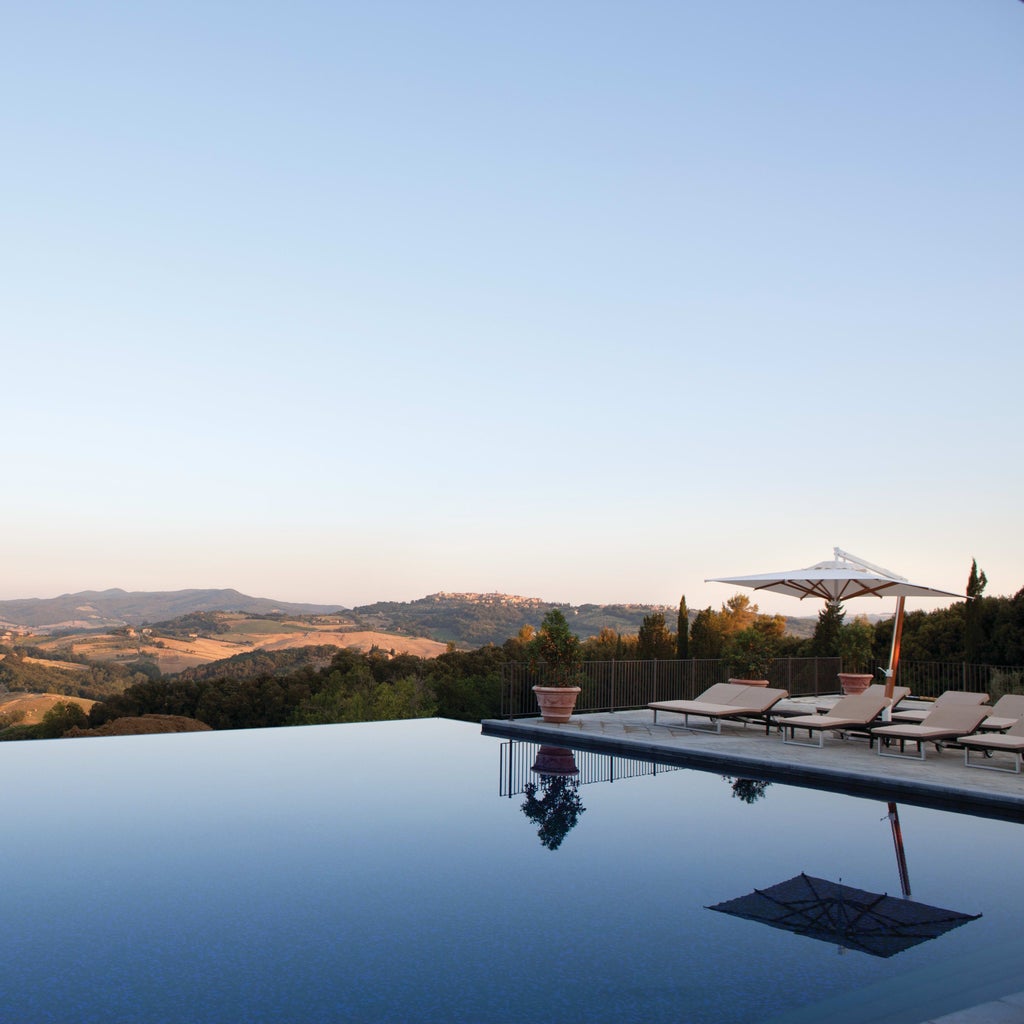 Medieval Italian castle hotel with stone walls and tower nestled on hilltop amongst cypress trees at golden sunset in Tuscany