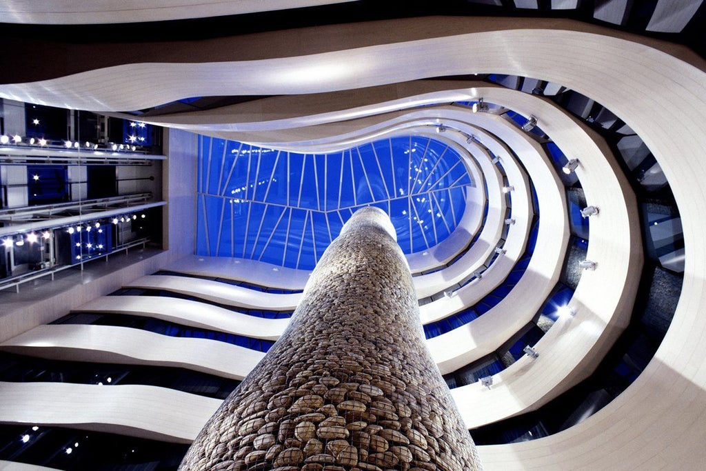 Modern luxury hotel exterior with curved glass facade, illuminated at dusk, reflecting city lights against a deep blue sky in Bilbao