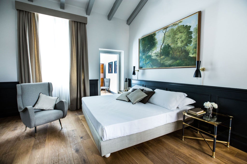 Elegant Deluxe Room at SoprArno Suites, featuring plush bedding, antique wooden furnishings, and soft natural light illuminating rustic Italian design details.