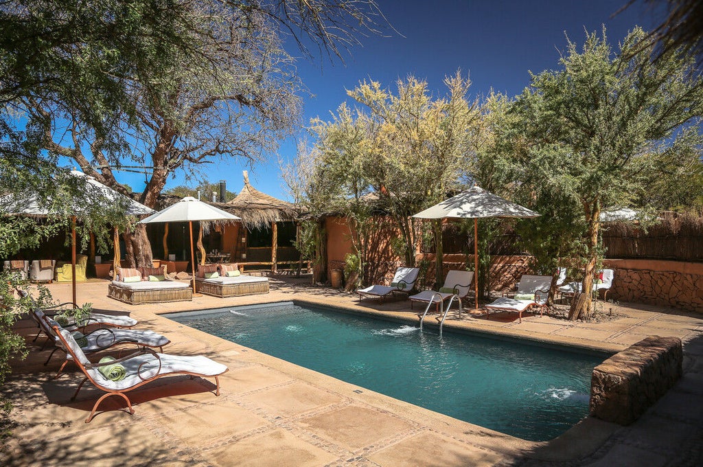 Desert resort villa with adobe walls, thatched roof, and private wood terrace surrounded by native cacti and mountains at dusk