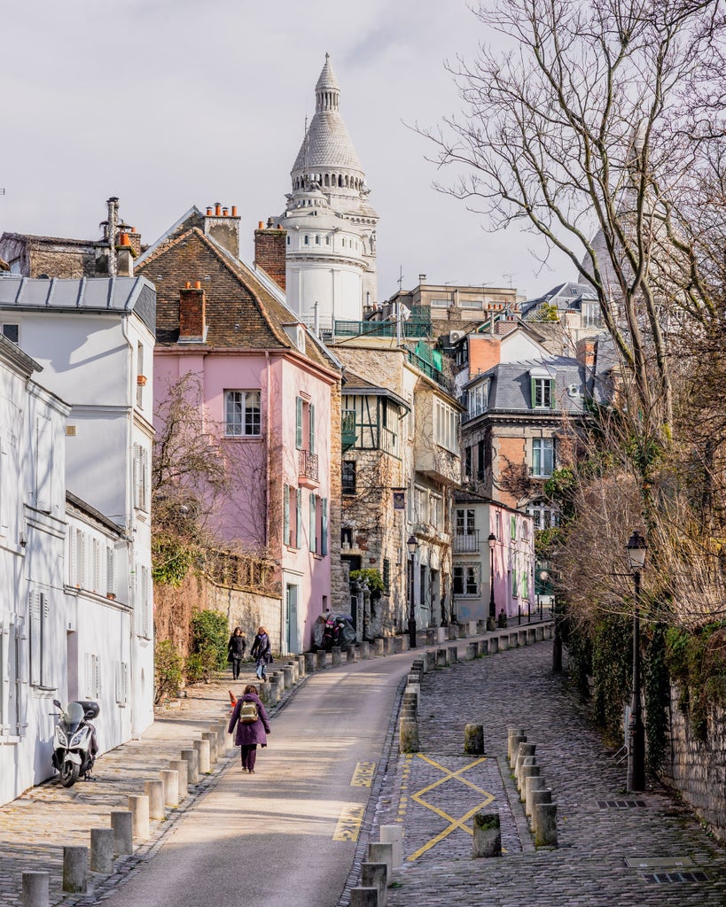 Cobblestone streets of Montmartre, Paris, with Sacré-Cœur Basilica backdrop, bohemian artists painting, and charming café terrace under soft golden light