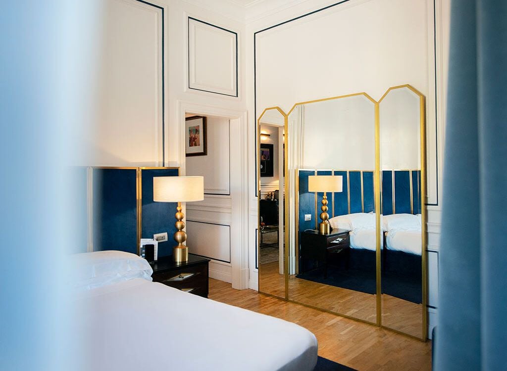 Elegant marble-clad luxury suite with panoramic windows, plush king bed, contemporary Italian design, and soft neutral color palette in prestigious European hotel