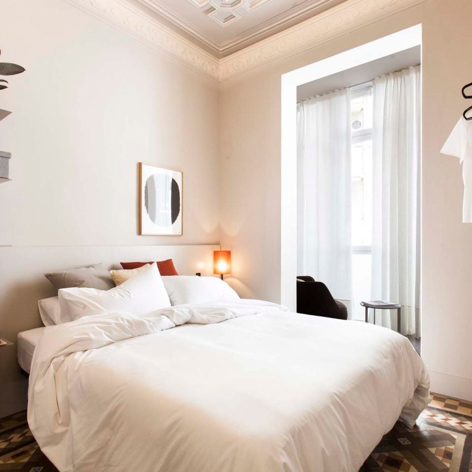 Luxurious Barcelona hotel room with modern minimalist design, crisp white linens, sleek wooden furniture, and soft ambient lighting creating a serene urban retreat atmosphere