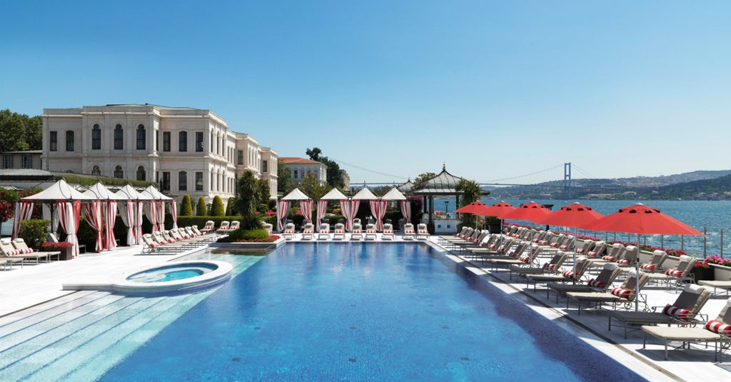 Elegant Ottoman-era palace hotel on Bosphorus waterfront with ornate white facade, manicured gardens and luxury terrace dining area