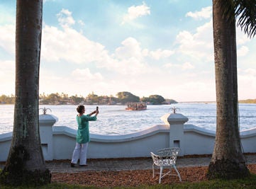 Colonial-style luxury hotel on Kochi waterfront with white facade, arched windows, wooden balconies and traditional sailing boats nearby