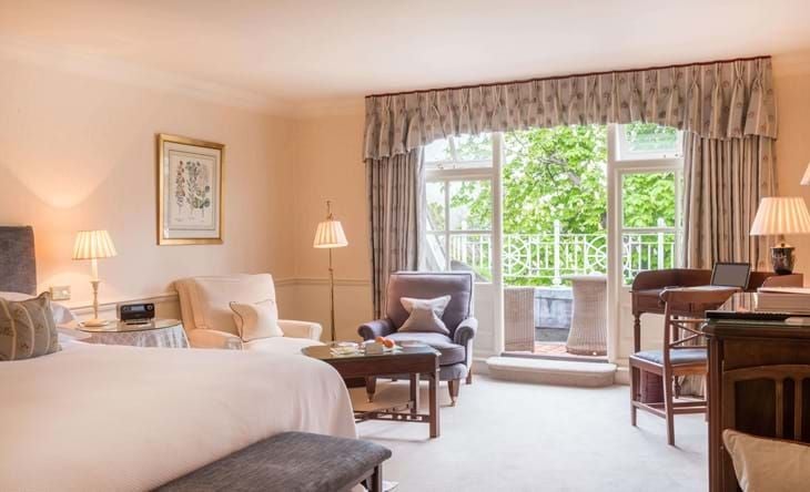 Elegant classic room with soft neutral tones, plush white bedding, sophisticated furnishings, and large windows overlooking lush greenery at Chewton Glen Hotel & Spa.