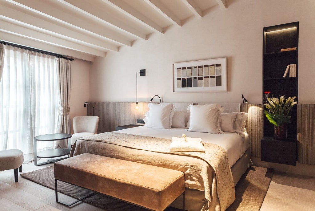 Elegant hotel room with minimalist design, featuring white walls, wooden floors, luxurious king-sized bed, and artistic decor in a historic Spanish setting