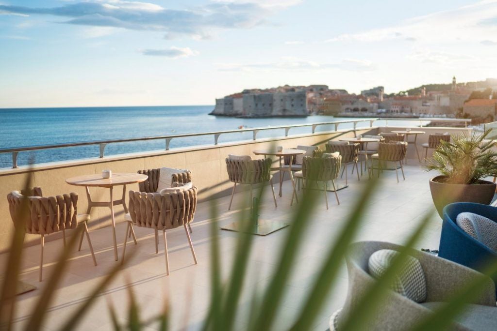 Modern beachfront hotel featuring curved white architecture with balconies, nestled between crystal blue Adriatic Sea and mountains