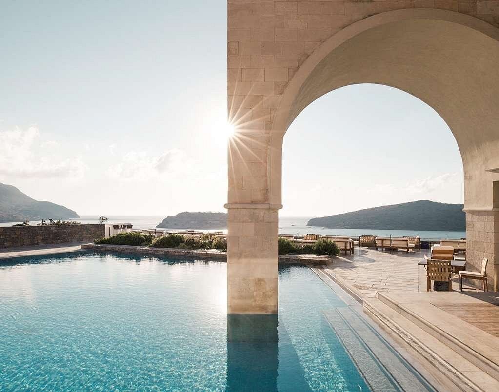 Luxurious infinity pool overlooking the Aegean Sea at Blue Palace resort, with stone terraces and traditional Greek architecture at sunset