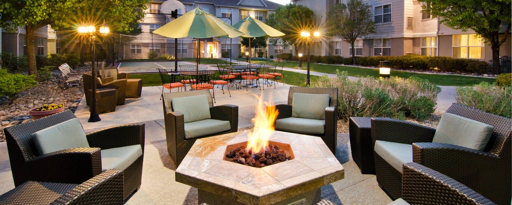 Modern hotel exterior with tan and brown facade, featuring glass windows, covered entrance and well-manicured landscaping at dusk