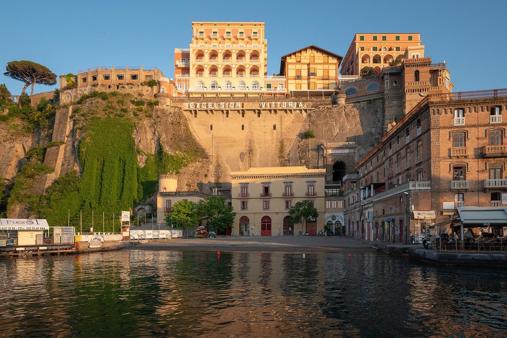 Elegant Italian coastal hotel with white stone facade, arched windows and balconies overlooking the Mediterranean Sea at sunset