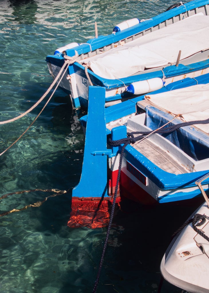 Fishing boat anchored in turquoise Taormina Bay with Mount Etna volcano backdrop, golden sunlight illuminating crystal waters