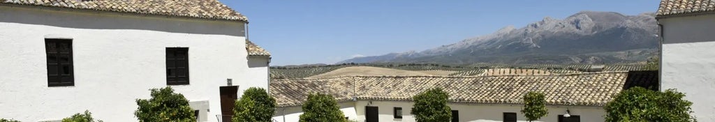 Historic Spanish luxury hotel with white-washed walls, terracotta roof, lush gardens, and mountain backdrop at golden hour