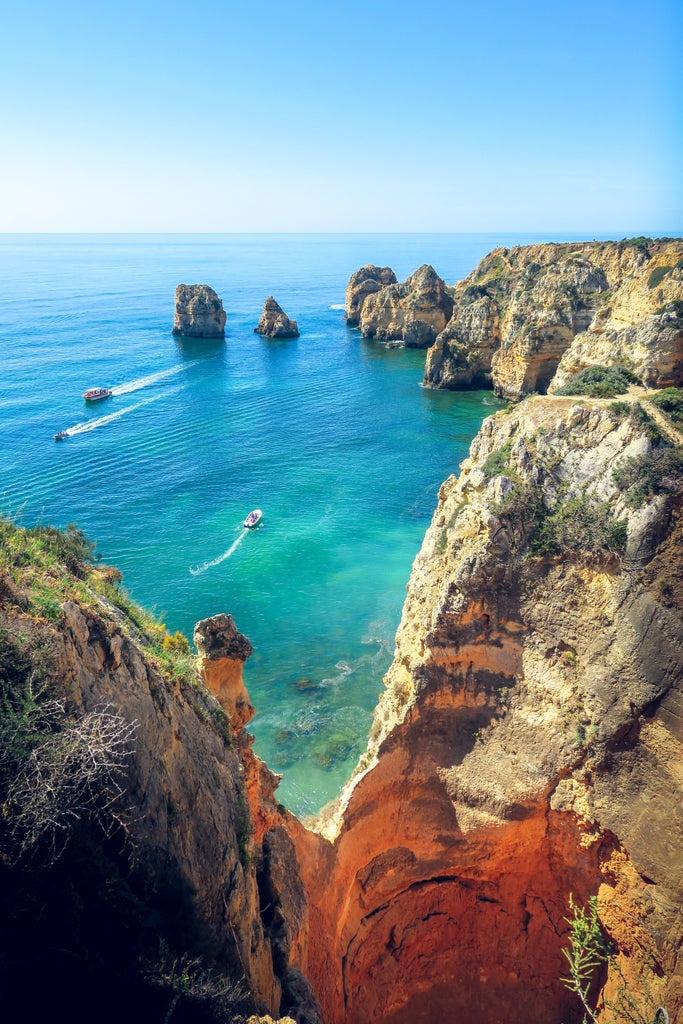 Dramatic oceanfront cliffs of Portugal's Algarve coast at sunset, with luxury villas perched along rugged limestone formations above blue waters