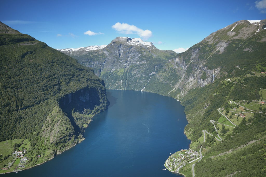 Scenic Norwegian fjord with dramatic cliffs, cascading waterfalls, and a luxurious cruise boat gliding through the emerald-green Geirangerfjord landscape