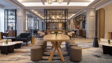 Modern glass-fronted Tirana Marriott hotel with elegant black-and-gold facade, illuminated entrance, and manicured landscaping at dusk