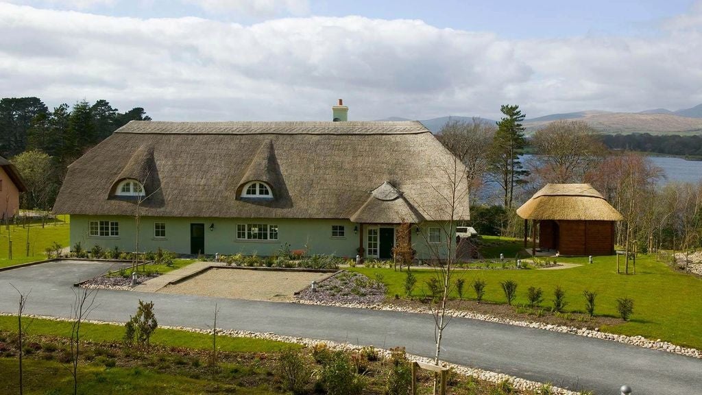 Spacious coastal villa bedroom with panoramic bay windows, king bed, elegant furnishings, and white linens overlooking Irish waters