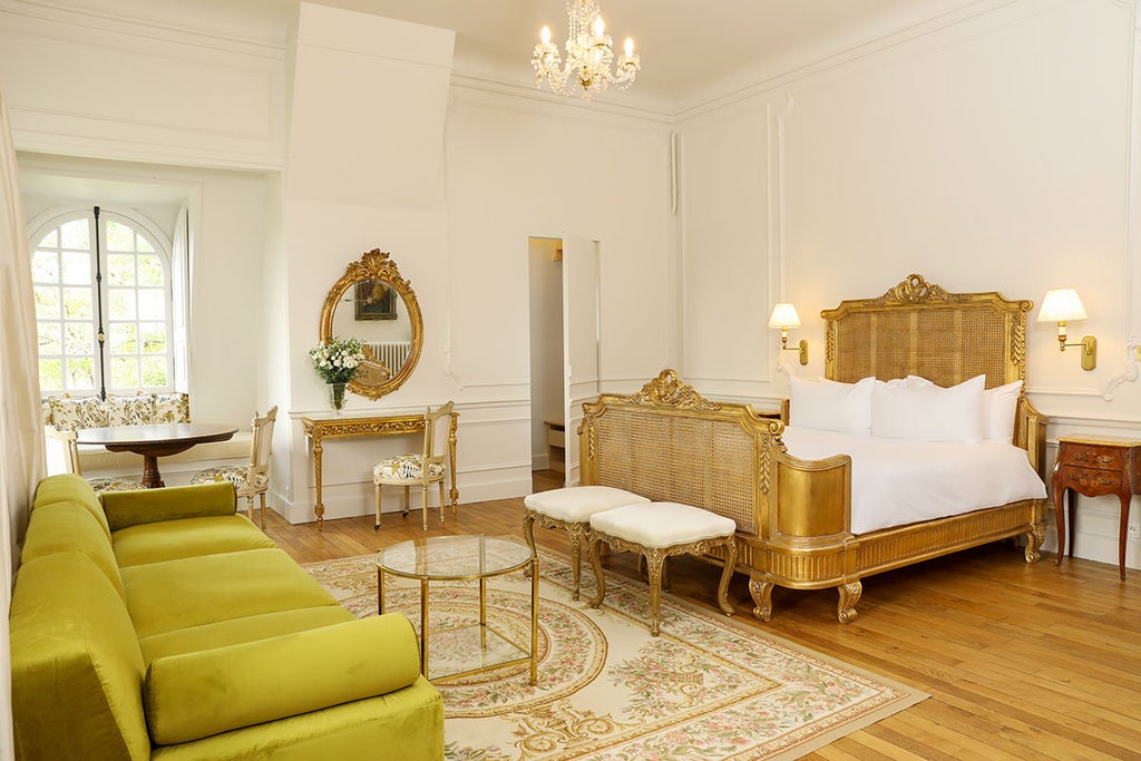 Elegant corner king room with ornate crown molding, crystal chandelier and floor-to-ceiling windows overlooking French château gardens