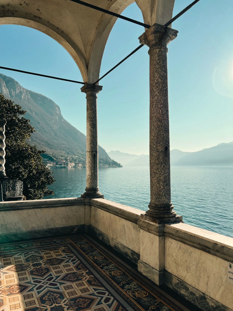 Beautiful Lake Como shoreline with luxury villas nestled among cypress trees, reflecting in tranquil waters under a golden Italian sky.