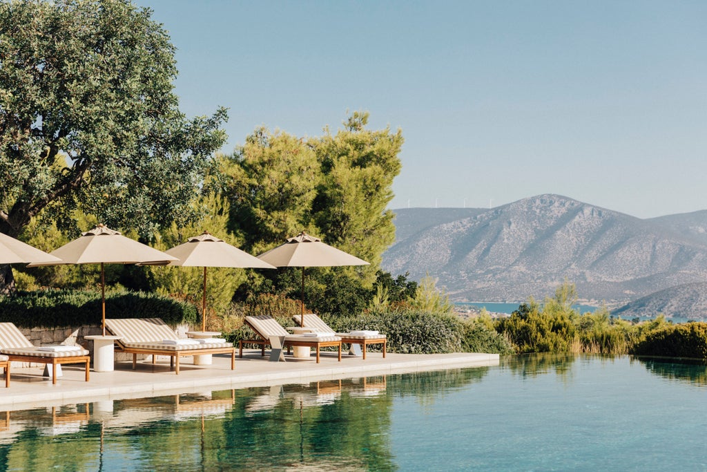 Pristine white Greek pavilions with private pools nestled into a hillside, overlooking the Aegean Sea against a clear Mediterranean sky