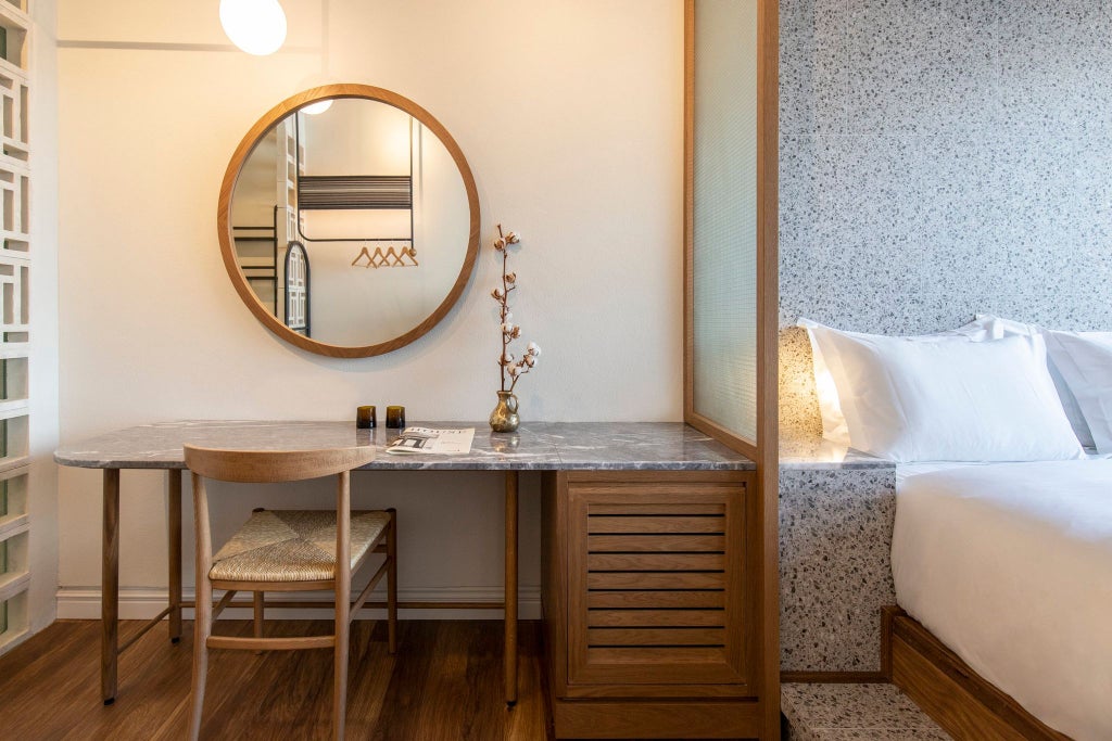 Modern minimalist hotel room with warm wooden floors, crisp white linens, and large windows offering natural light in a sophisticated Athens boutique setting.