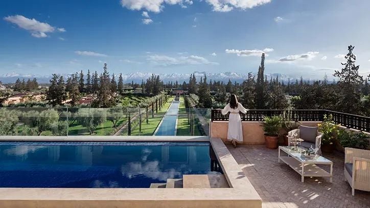 Elegant Moroccan-style royal suite with white-draped four-poster bed, private plunge pool, and arched windows overlooking lush gardens at luxurious scenset resort