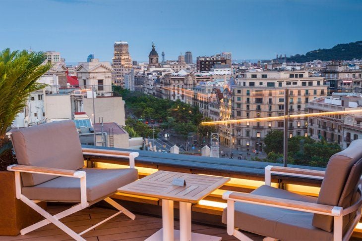 Elegant five-star hotel facade with ornate balconies, classical architecture and manicured palm trees along Barcelona's Passeig de Gràcia