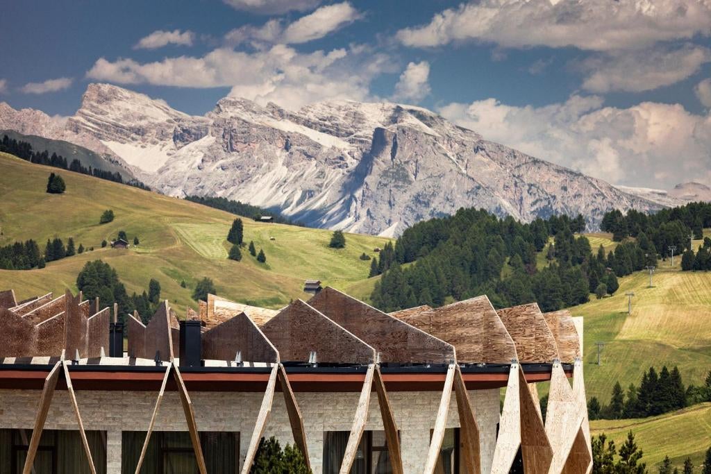 Modern mountain resort with glass facade nestled in snowy Dolomites, featuring panoramic windows and sleek wood-stone architecture