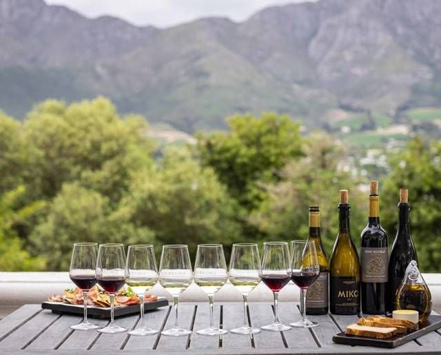 Luxurious vineyard hotel nestled in scenic South African mountains, with elegant white buildings, lush green landscape, and panoramic Franschhoek valley views