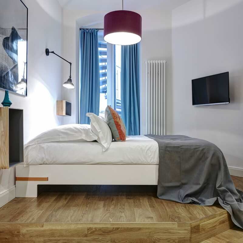 Elegant modern hotel room with minimalist design, plush white bedding, sleek wood furnishings, and large windows overlooking urban German landscape