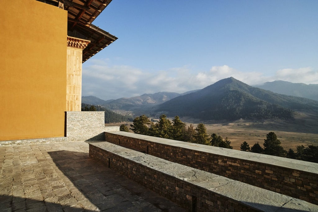 Luxurious hillside lodge with floor-to-ceiling windows overlooking misty Bhutanese valley, featuring timber and stone architecture